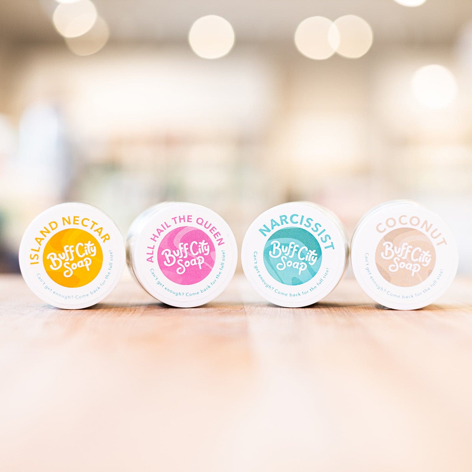 Four Mini Body Butter Containers with varied lid colors on side and lined up on wooden counter